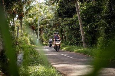 BALI, INDONESIA - DECEMBER 26, 2018: Young couple riding scooter in the rainforest, Bali island.