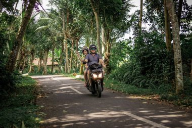 BALI, INDONESIA - DECEMBER 26, 2018: Young couple riding scooter in the rainforest, Bali island.
