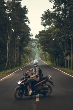 Ağaçların arasında yolda scooter üzerinde genç kadın. Bali Adası.