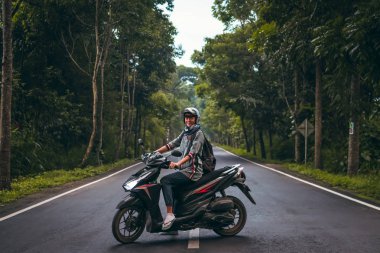 Ağaçların arasında yolda scooter üzerinde genç kadın. Bali Adası.