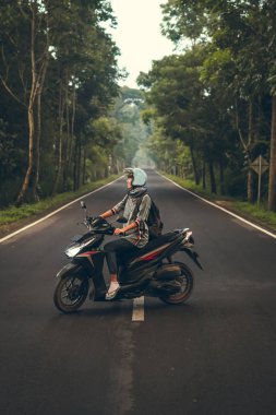 Ağaçların arasında yolda scooter üzerinde genç kadın. Bali Adası.