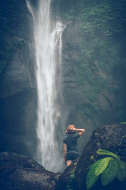 Young woman posing on a great Sekumpul waterfall in the deep rainforest of Bali island, Indonesia.