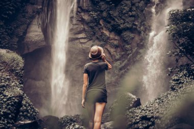 Young woman posing on a great Sekumpul waterfall in the deep rainforest of Bali island, Indonesia.