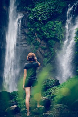 Young woman posing on a great Sekumpul waterfall in the deep rainforest of Bali island, Indonesia.