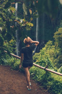 Young woman posing on a great Sekumpul waterfall in the deep rainforest of Bali island, Indonesia.