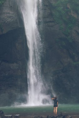 Young woman posing on a great Sekumpul waterfall in the deep rainforest of Bali island, Indonesia.