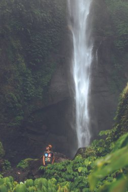 Young woman posing on a great Sekumpul waterfall in the deep rainforest of Bali island, Indonesia.