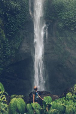 Young woman posing on a great Sekumpul waterfall in the deep rainforest of Bali island, Indonesia.