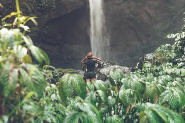 Young woman posing on a great Sekumpul waterfall in the deep rainforest of Bali island, Indonesia.