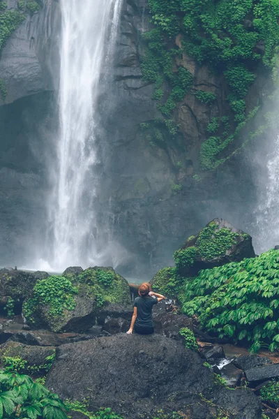 Jovem posando em uma grande cachoeira Sekumpul na floresta tropical profunda da ilha de Bali, Indonésia . — Fotografia de Stock