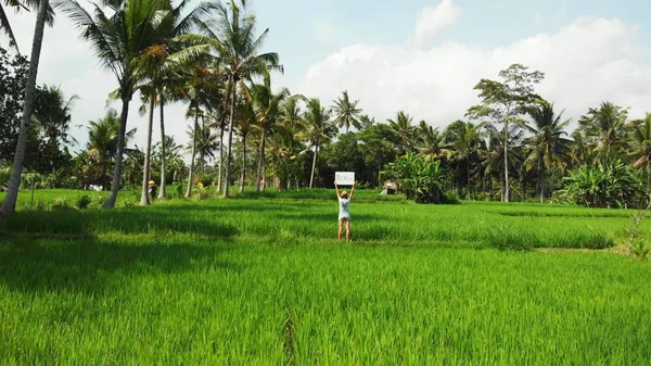 Jeune femme à l'extérieur avec tableau blanc et mot d'écriture tropicale sur elle. Des images de drones volants. Fond tropical vert brillant. Beau concept de voyage tropical. Bali île . — Photo
