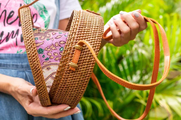 De handen van de vrouw met stylich eco vriendelijke rotan zak op een tropische achtergrond. Bali eiland. — Stockfoto