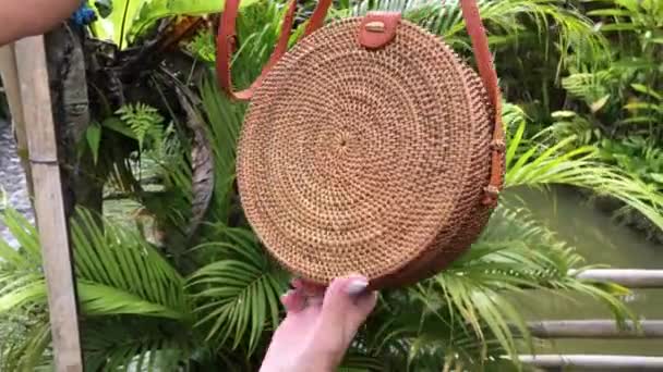 De handen van de vrouw met stylich eco vriendelijke rotan zak op een tropische achtergrond. Bali eiland. — Stockvideo