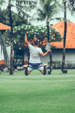 Genç freelancer adam tropikal park Bali adasında dizüstü bilgisayar ile atlama.