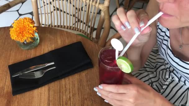 Mujer joven bebiendo un cóctel rojo en el restaurante de la isla de Bali, Indonesia. Imágenes 4K . — Vídeo de stock