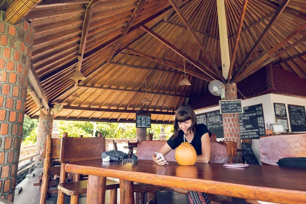 Mujer joven sentada en un café tropical con coco. Isla de Bali . —  Fotos de Stock