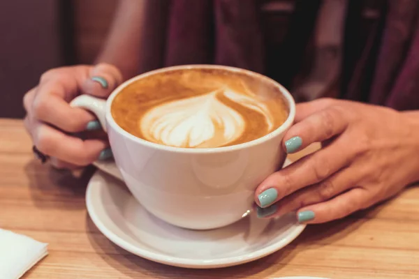 Młoda kobieta ręce z gorące latte na podłoże drewniane. Restaurant. Kubek gorącej kawy. — Zdjęcie stockowe