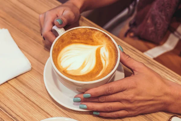 Młoda kobieta ręce z gorące latte na podłoże drewniane. Restaurant. Kubek gorącej kawy. — Zdjęcie stockowe