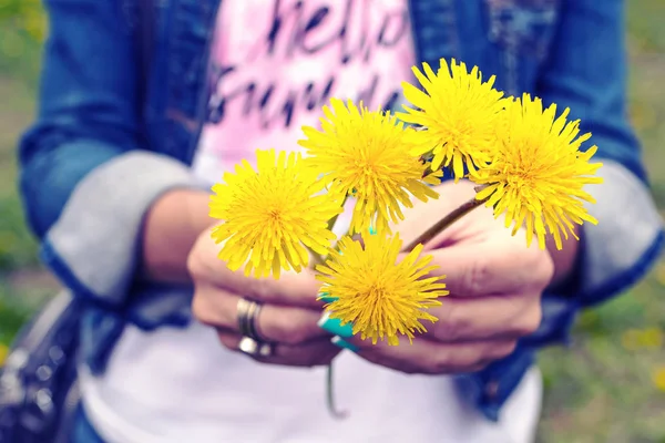 春天的时候,一个年轻的女人拿着蒲公英花束在绿色的公园里. 明亮而新鲜的花朵背景. — 图库照片