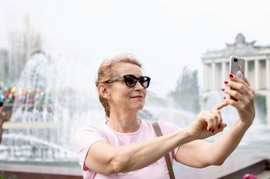Moskova, Rusya - 31 Mayıs 2019: Orta yaşlı kadın açık havada, bir çeşme arka plan üzerinde selfie çekerken.
