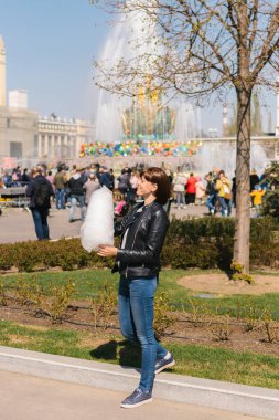 Çeşmeye yakın parkta pamuk şeker tutan gülümseyen heyecanlı bir kızın portresini kapatın.