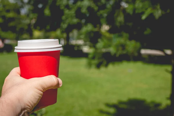 Férfi kéz kezében piros kávé papír pohár, életmód nyári lövés. — Stock Fotó
