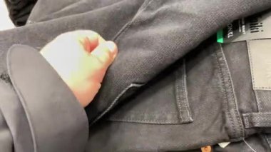 Erkek eli dükkanda siyah kot pantolon seçer..