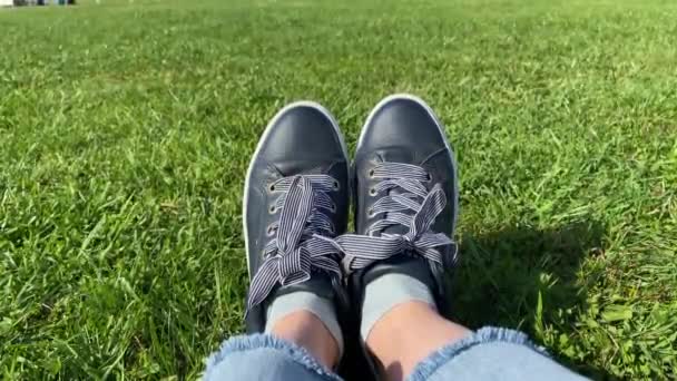 Pies femeninos en zapatillas de deporte gumshoes en una hierba verde iluminada por el sol, de cerca. — Vídeo de stock