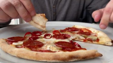Adam salamlı, biberli ve mozzarella peynirli pizza yiyor..