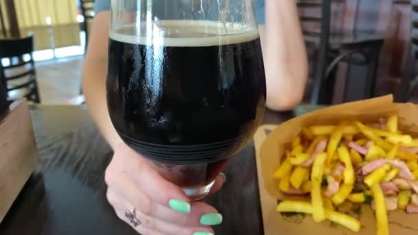 Mujer joven bebe una cerveza oscura en el bar. — Vídeo de stock