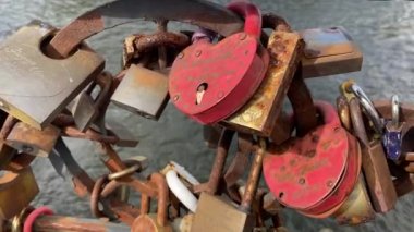 Güzel bir tarla derinliği ve arka planda bir nehir olan bir köprüdeki aşk asma kilitlerinin yakın görüntüsü. El kamerasıyla..