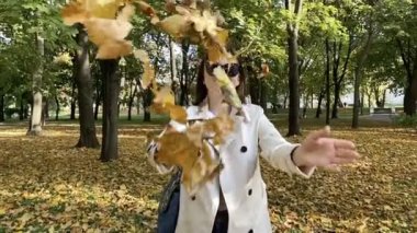 Genç kaygısız kadın sonbahar parkına yapraklar fırlatıyor. Yavaş çekim.