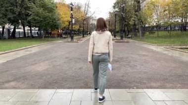 Genç kadın sonbahar parkında tıbbi koronavirüs maskesini çıkarıyor. Özgürlük kavramı.