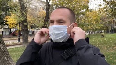 Genç adam parktaki tıbbi koronavirüs maskesini çıkarıyor. Yavaş çekim.