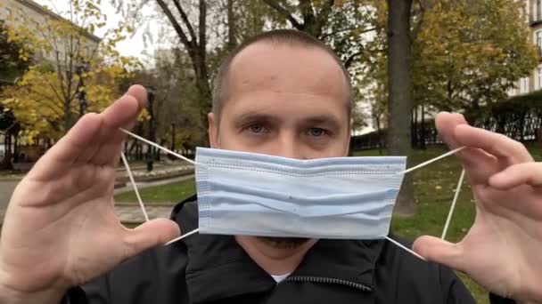 Young man takes off the medical coronavirus mask in the park. Slow motion. — Stock Video