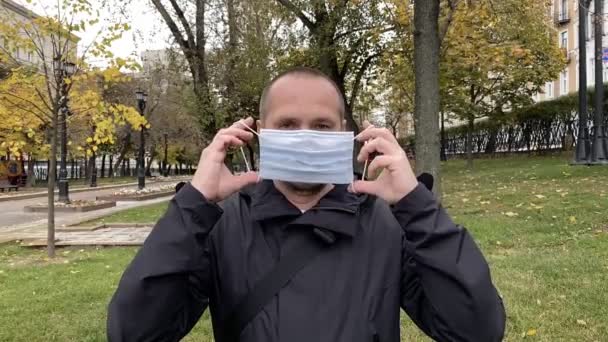 El joven se quita la máscara del coronavirus médico en el parque. Movimiento lento. — Vídeos de Stock