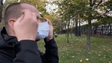 Genç adam parktaki tıbbi koronavirüs maskesini çıkarıyor. Yavaş çekim.