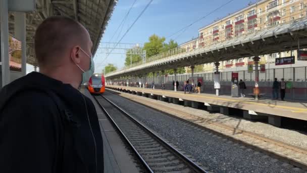 MOSKVA, RUSKO - 5. října 2020: Muž s lékařskou maskou stojí na vlakovém nádraží, zatímco vlak přijíždí. — Stock video