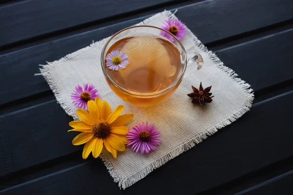 Květinové čaje v šálku transparentní sklo na černém stole. Léčivé čaje. — Stock fotografie