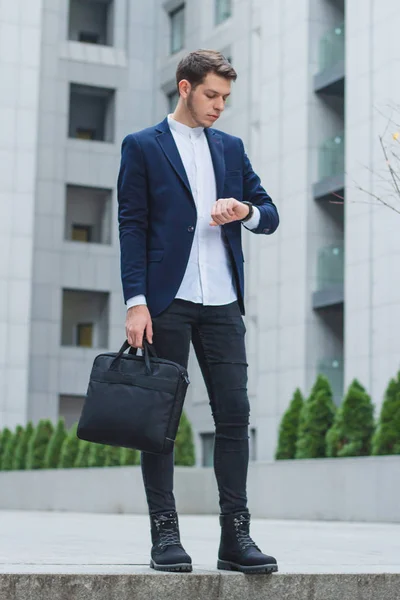Geschäftsstil. Jungunternehmer in der Hand die Aktentasche. der Typ in der blauen Jacke schaut auf seine Uhr. — Stockfoto