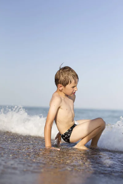 少年は ビーチに座っているし 波で遊ぶ ビーチでバカンスの子 — ストック写真