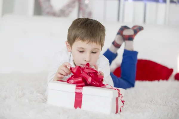 A little boy lying on the bed opens a gift. Get a box with a gift