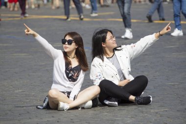 Rusya, Moskova, 29 Temmuz 2018. Kızıl Meydan. Genç kızlar asfaltta oturuyorlar. Turistler simgesel yapılara işaret ediyor
