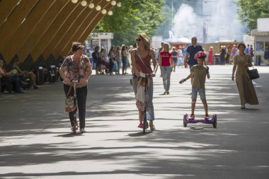 Rusya, Moskova, 29 Temmuz 2018. Sokolniki Parkı. Büyükanne anne ve torunu scooter yolda sürme. Scooter'da aile