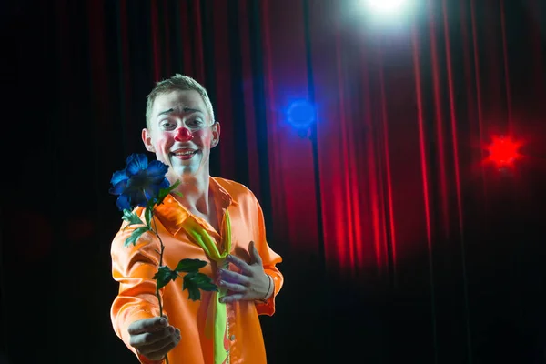 Circus clown performs number. A man in a clown dress with a flower