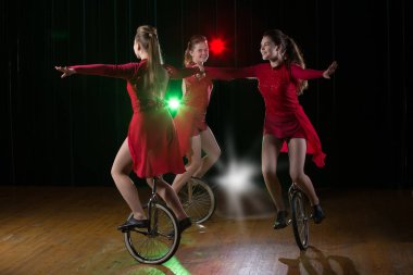 Monocycle'daki üç kız sahnede performans sergiliyor. Bisikletli Sirk Sanatçıları