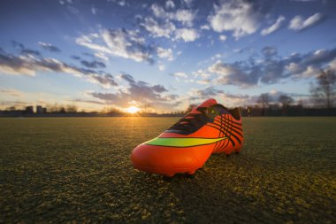 Gün batımında sahanın arka planında spor ayakkabılar. Spor ayakkabıile futbol sahası