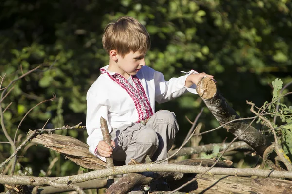 一个穿绣花衬衫的男孩坐在木头上 乌克兰或白俄罗斯儿童 — 图库照片