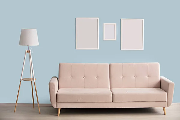 Minimalist interior. Sofa lamp picture frames on a blue wall background.