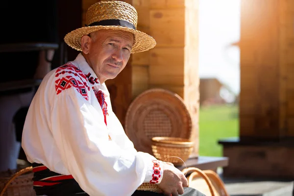 Um artesão de Belarusian ou Ukrinsky na camisa bordada tece cestas do latido de vidoeiro. O homem faz cestos de bétula. — Fotografia de Stock